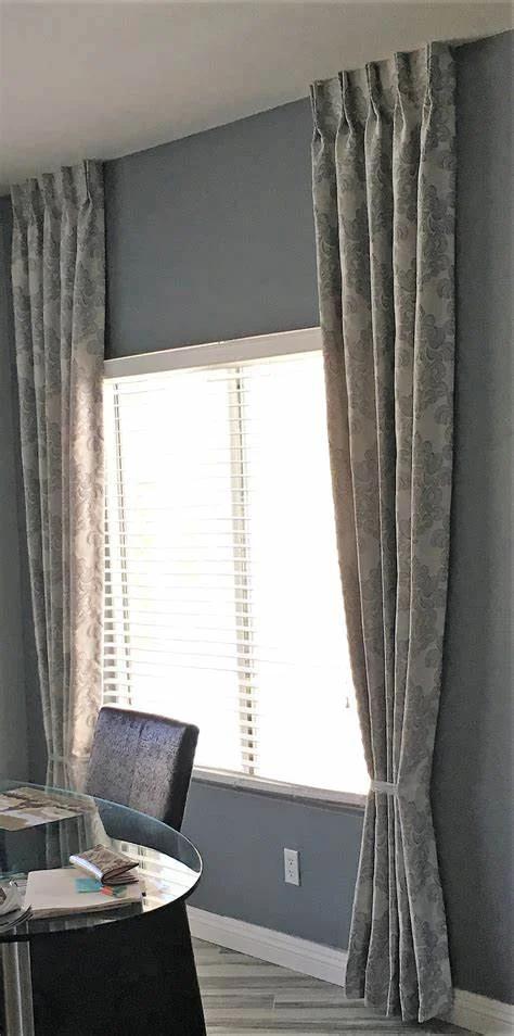 Custom board-mounted drapery with elegant pleats framing a window with blinds in a modern dining area